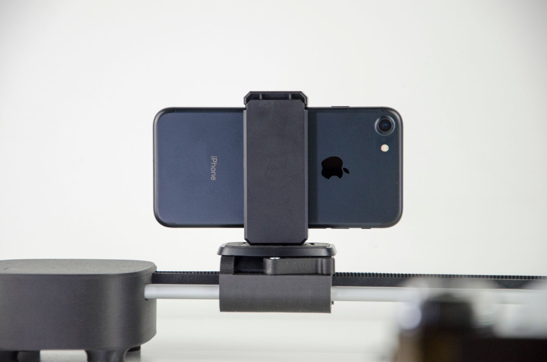 Smartphone scuro montato su un supporto, ripreso di fronte su uno sfondo bianco.